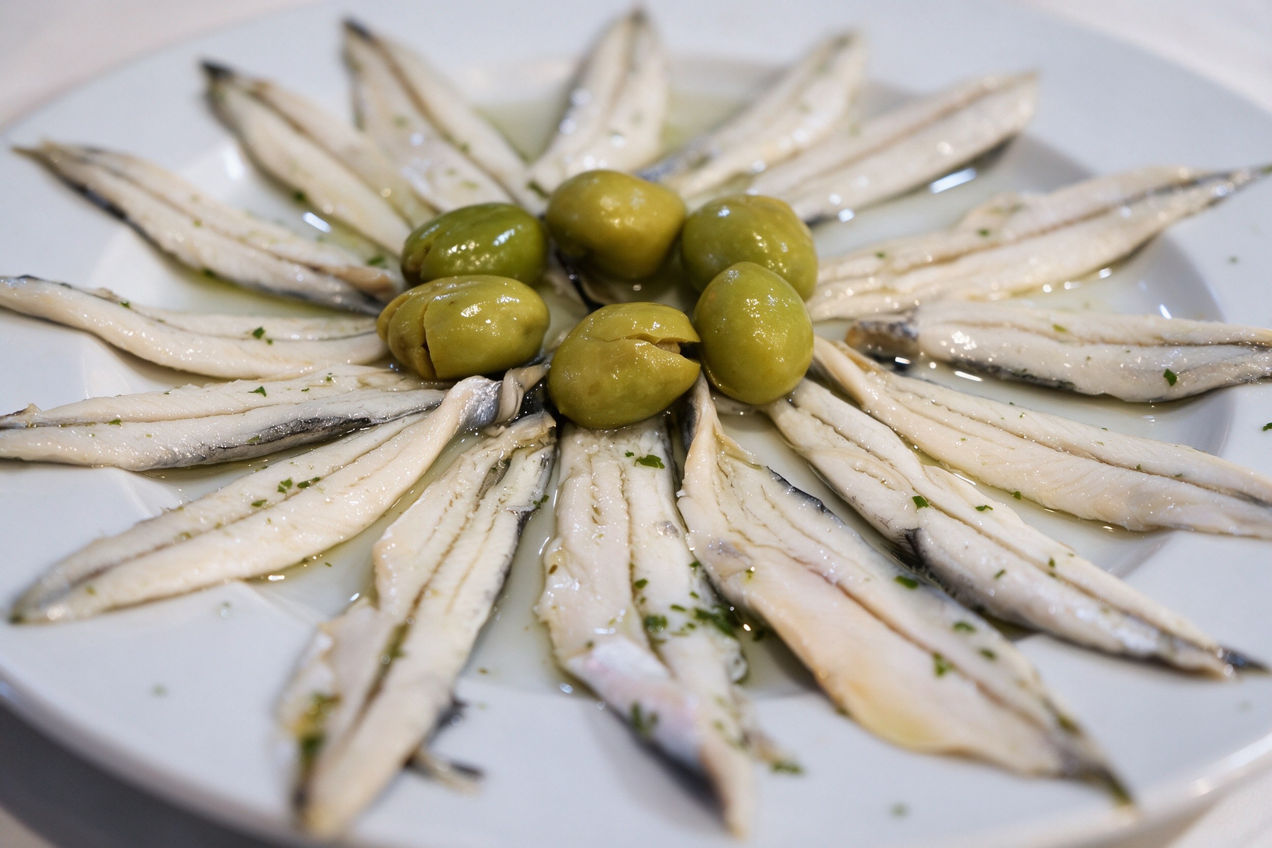 Boquerones en vinagre dispuestos en abanico con aceitunas en plato blanco