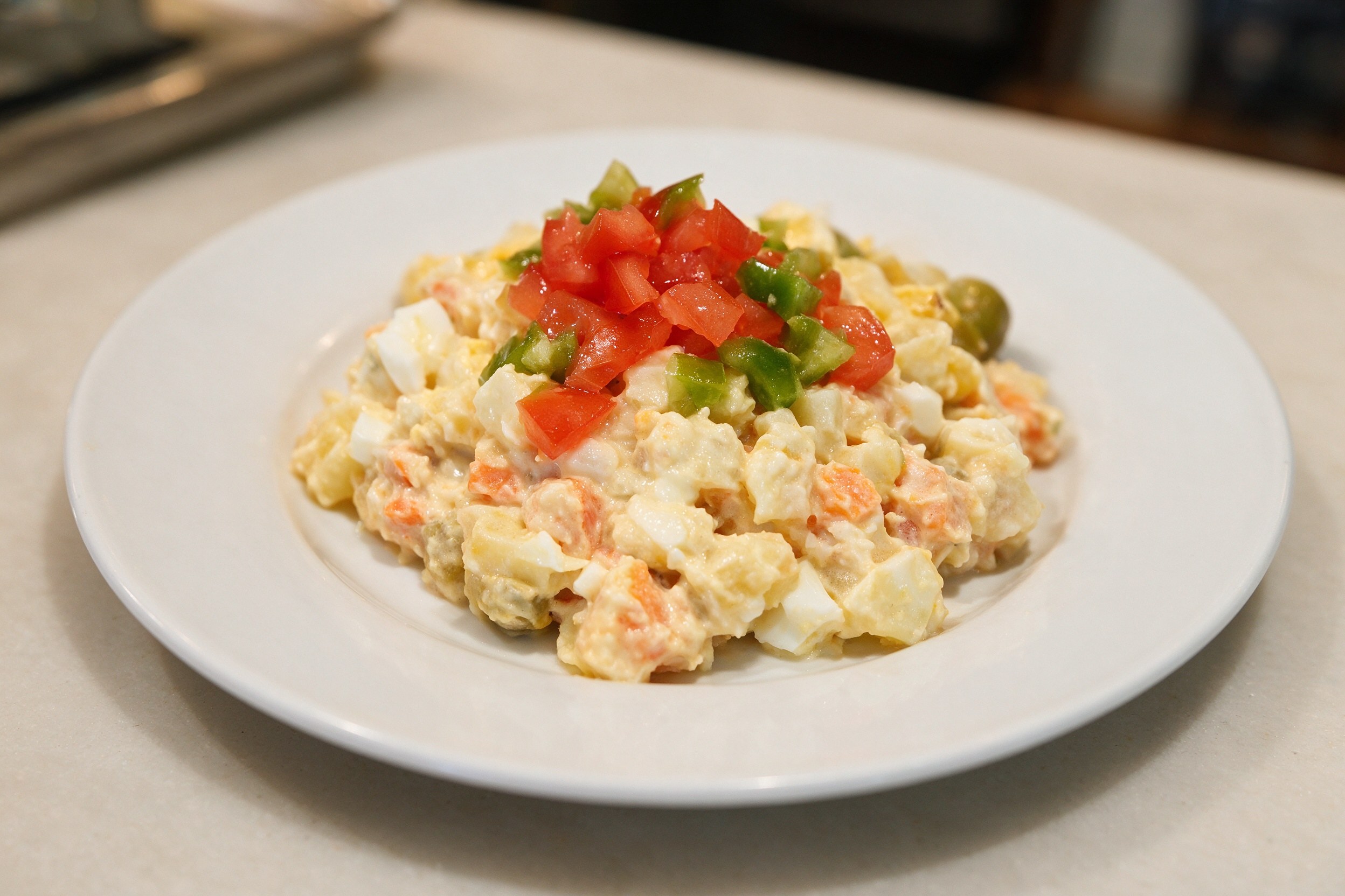 Ensaladilla rusa coronada con tomate y pimiento verde en plato blanco